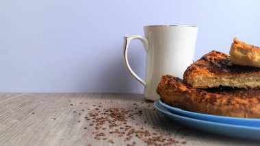 Beyaz porselen bardaklı mavi bir tabak üzerinde doğu ekmeği ve beyaz arka plandaki ahşap bir masada keten tohumları.