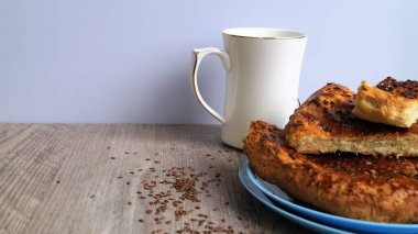 Beyaz porselen bardaklı mavi bir tabak üzerinde doğu ekmeği ve beyaz arka plandaki ahşap bir masada keten tohumları.