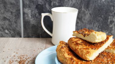 Beyaz porselen bardaklı mavi bir bulaşık ve siyah arka plandaki ahşap bir masada keten tohumlar.