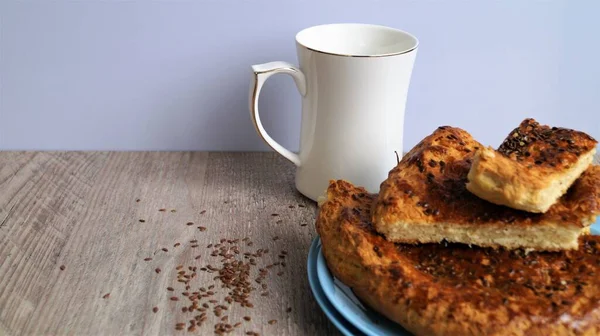 oriental bread on a blue dish with white porcelain mug and linen seeds on a wooden table on white background