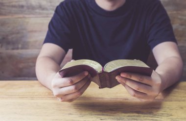 Bir adamın el ele tutuşması ve kutsal İncil 'i ahşap masada okuması. Kopya alanı olan Hıristiyan arka planı.