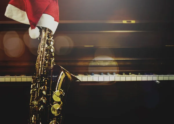 Piyano anahtarları ve Noel Baba fıkralı saksafon. Piyano tuşlarında gece yarısı şapka. Fotokopi alanı olan Noel müziği arka planı.
