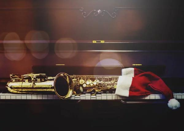 Piyano anahtarları ve Noel Baba fıkralı saksafon. Piyano tuşlarında gece yarısı şapka. Fotokopi alanı olan Noel müziği arka planı.