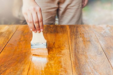 Bir adamın ellerini boya fırçasıyla kapatır ve ahşap masa zeminine iğrenç cila çizer..