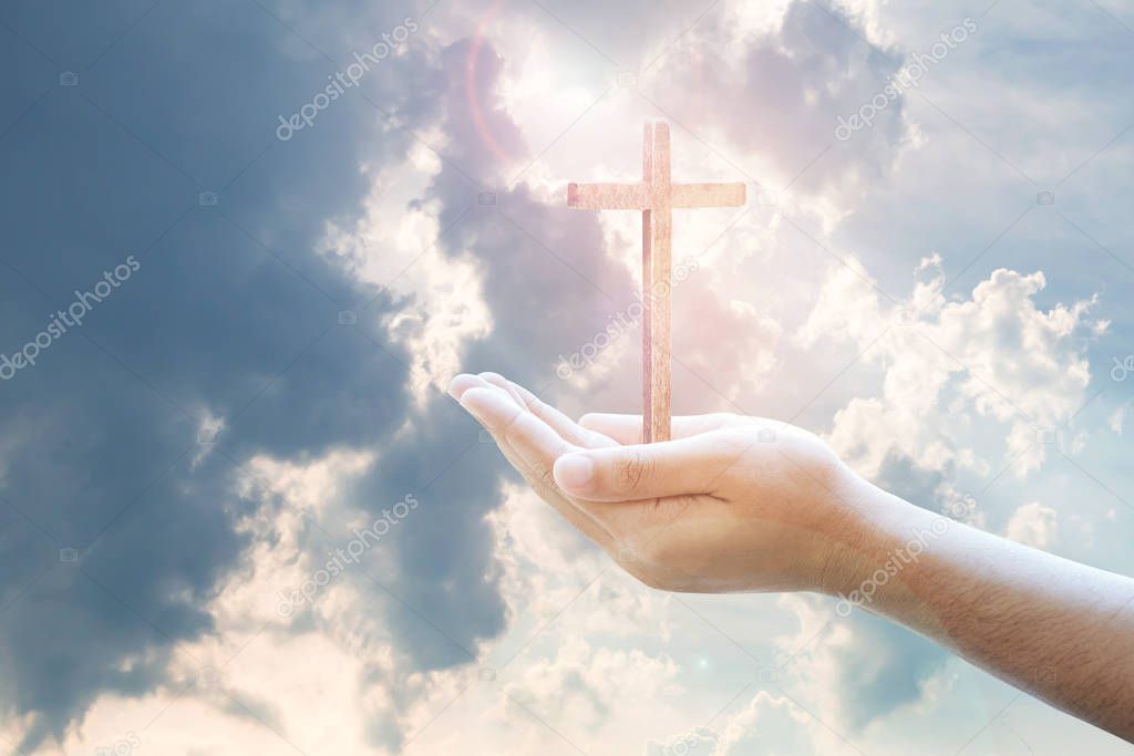 conceptual image of man hands holding the wooden cross over cloudy blue sky background