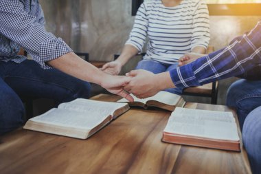 Hıristiyan grup el ele tutuşup kutsal İncil 'le ahşap bir masanın etrafında dua ediyor.