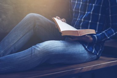 Bir adamın elinde İncil 'i tutarken ve okurken tahta bir sandalyede otururken, Hıristiyan arka planında