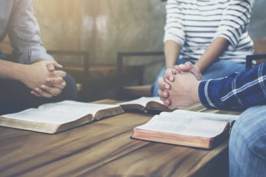 Bir grup Hıristiyan, ahşap bir masanın etrafında oturuyorlar. Bulanık İncil sayfası açıp Tanrı 'ya birlikte dua ediyorlar.