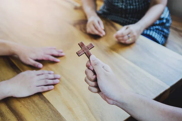 İsa 'nın hikayesini anlatırken ve inançsız arkadaşlarına ahşap masa etrafında İncil' i anlatırken elinde küçük ahşap bir haç tutan genç Hristiyan 'ın yakın çekimi. Büyük komisyon kavramı..