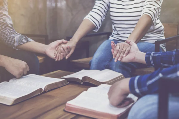 Küçük bir Hıristiyan grup ahşap bir masanın etrafında el ele tutuşup dua ediyor. Sınıf, bağlılık veya dua toplantısı kavramında bulanık bir İncil sayfası var.