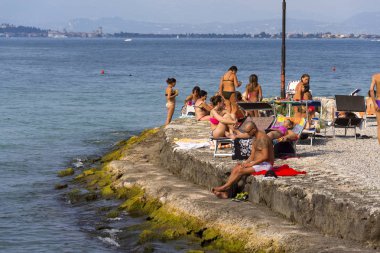 Bir Desenzano del Garda, İtalya için plajda güneşlenirken insanlar.