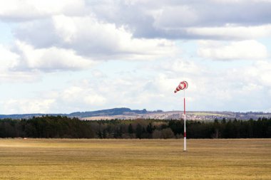 Boş çimenlik hava sahasında kırmızı ve beyaz rüzgarlı çorap, arka planda dramatik bulutlar, rüzgarlı hava tahmini ve hava trafik konsepti