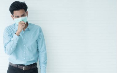 Asyalı bir adamın kurumsal ofisinde, kısa saçlı, mavi uzun Jan gömlekli, bol pantolonlu, siyah kuşaklı, hastalık mikroplarından ve tozdan korunmak için yeşil bir maske takıyor..