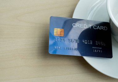 The blue cedit card is placed near the coffee cup on a wooden table, suitable for the digital cashless era.