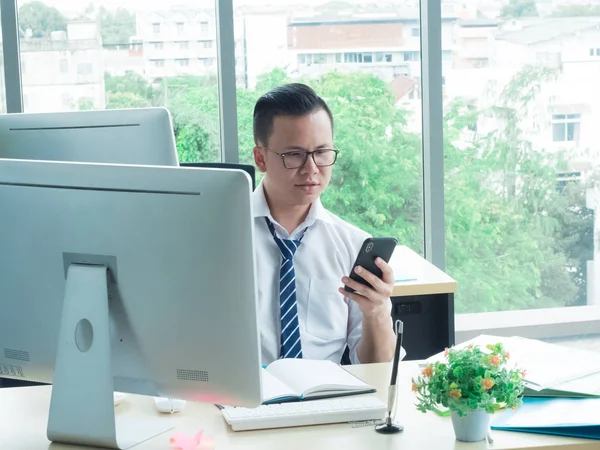 In the office of a company, employees wear necktie, glasses in front of their work, in front of computers, look at mobile phones to make an appointment for customers and contact meetings. Work hard