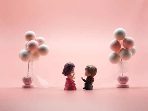 Couple toy dool boyfrend Kneel to propose just married surprise romantic girlfriend.Male Hand over the ring female between Two balloon and pink white isolate background 14 fourteen feb Valentine