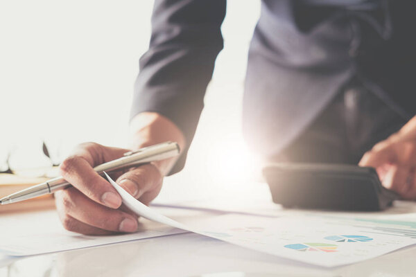 Close up of businessman or accountant hand holding pen working on calculator to calculate business data, accountancy document and laptop computer at office, business concept