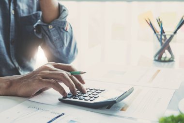İş adamı ya da muhasebecinin el ele tutuşma kalemini kapat. İş verilerini, muhasebe belgelerini ve ofisteki dizüstü bilgisayarları hesaplamak için hesap makinesi üzerinde çalış.