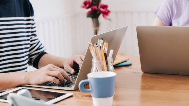 Yakın plan grafik tasarım ekibi, ahşap çalışma masasında bilgisayar dizüstü bilgisayar ve tabletle birlikte rahat oturma odası üzerinde çalışıyorlar..
