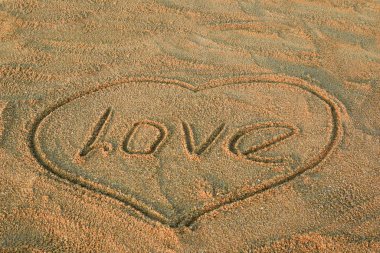 Kalp ve aşk kelimesi kuma çizildi. Plaj arka planı. Kapat.