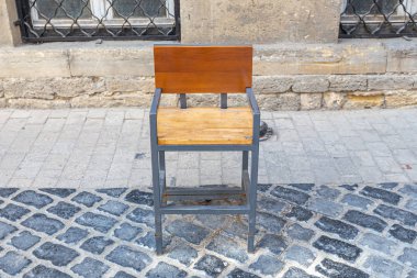 Tahta koltuklu metal sandalye ve kaldırım taşlarının arkası.