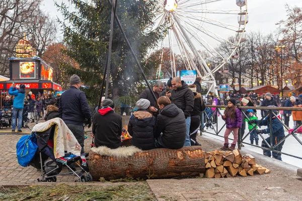 La gente se sienta en un tronco y disfruta del fuego en un parque de la ciudad — Foto de Stock