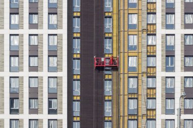 The worker works at height, in a red construction cradle