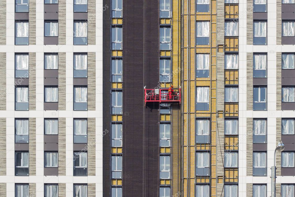 The worker works at height, in a red construction cradle