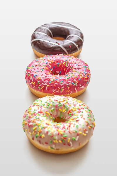 Three glazed doughnuts, with strawberry, vanilla and chocolate icing