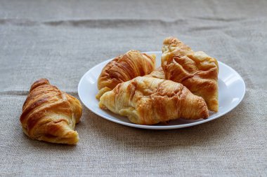 Geleneksel taze Fransız kruvasanı. Altın kabuklu. beyaz bir tabakta ve branda bir masa örtüsünde.