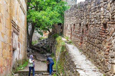 Ananuri, Georgia, 07.20.2019. Kilisenin duvarı ve Ananuri kalesindeki kale duvarı. Bir kadın kiliseden çıkarken mendilini düzeltir, bir erkek sırt çantasıyla beceriksizce dolaşır.