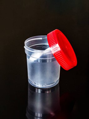 Kırmızı kapaklı şeffaf plastik kap ve analizler için beyaz kaşık, koyu bir arka planda.