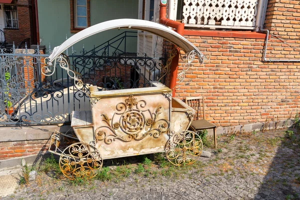 An abandoned metal counter, for sale, in the form of a carriage, rusted in the open air against the brick wall of the house