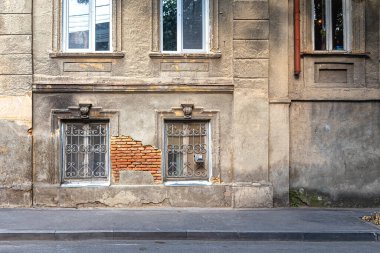 Eski bir evin duvarı. Pencereleri parmaklıklı ve birinci katta yangın izleri var. Düşen alçının altında eski tuğlalar var. Şehrin fakir mahalleleri