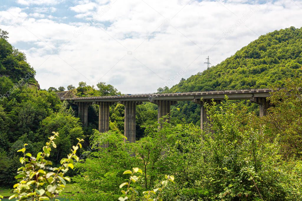 High bridge over the mountain river Arkala in Georgia. Cloudy sky and mountains covered with green trees
