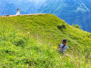 Dağların tepesinde, bir dağ geçidinde, fotoğrafçı bir düğün fotoğrafı çekiyor. Gelin ve damadın fotoğraflarını dağ manzaralarının arka planında çeker.
