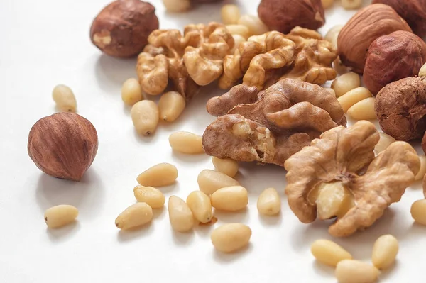 A mixture of walnuts, pine nuts and hazelnuts on a light background