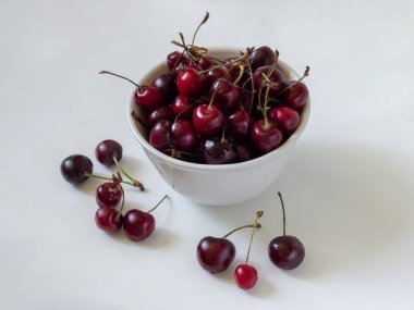 Beyaz seramik bir kupada olgun kirazlar, Kupadan birkaç dut düştü ve sıradaki yalan. Beyaz arkaplanda izole