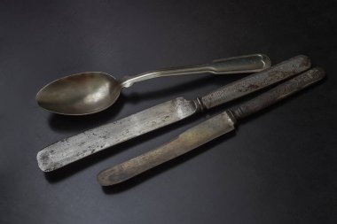 Kaşık ve iki bıçak eski çatal bıçak takımı siyah bir masada. 19. yüzyılın kısmen paslı bıçakları. Kabzasında oyma var.