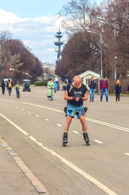 Moskova, Rusya, 04.20.2018. Şortlu yaşlı bir adam ve silindirli bir tişört akıllı telefonuna bakar, parktaki bisiklet yolunda sürmeye devam eder.