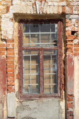 Pencerenin camları arasında parmaklıklar olan eski pencere çatlamış kahverengi boya, eski tuğla duvarlar.