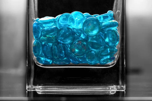 Glass turquoise stones shine in a glass vase. In black-and-white photography, the colored stones of the lampwork