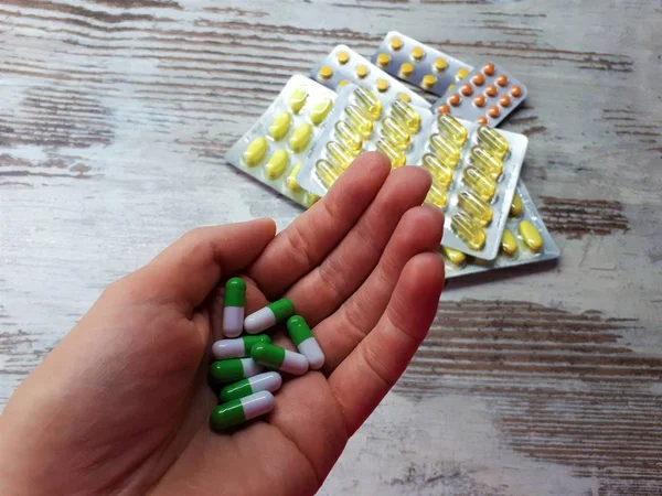 水疱における黄橙色の異なる医薬品を背景に緑白色の医薬品で手の手のひらの近くに — ストック写真