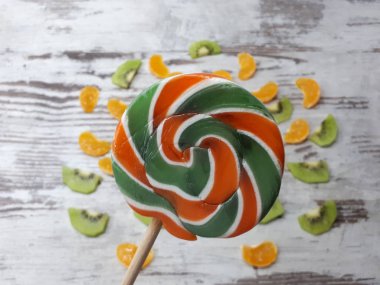 Dilimlerden, kivilerden, mandalinalardan oluşan büyük yuvarlak bir meyve lolipopunun yakın plan çekimi.