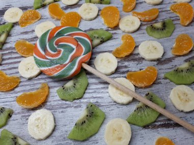  Dilimlenmiş muz, kivi, mandalina ve portakaldan oluşan büyük yuvarlak bir meyve lolipopunun yakın plan çekimi.