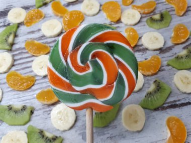  Dilimlenmiş muz, kivi, mandalina ve portakaldan oluşan büyük yuvarlak bir meyve lolipopunun yakın plan çekimi.