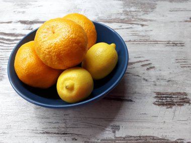 Meyvelerin yakın çekimi, olgun sulu mandalinalar ve ahşap bir arka planda mavi bir kasede sarı sağlıklı limonlar.