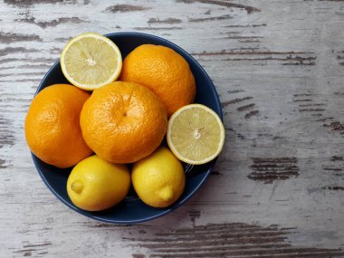 Meyvelerin yakın çekimi, olgun sulu mandalinalar ve ahşap bir arka planda mavi bir kasede sarı sağlıklı limonlar.