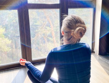  Açık tenli genç bir kız / kadın sabahları büyük bir panoramik pencerenin önünde nefes alma egzersizi / yoga yapıyor..