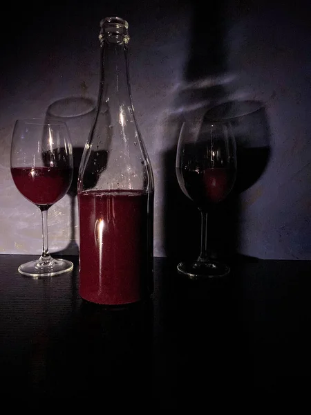 一瓶红酒和两杯酒杯倒立在黑色的表面上 背靠着一面抽象的蓝色墙 自由自在的空间 — 图库照片